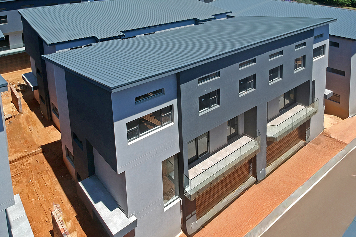Aerial view of a modern multi-story residential complex featuring contemporary architectural design, corrugated metal roofing, and glass balcony balustrades.