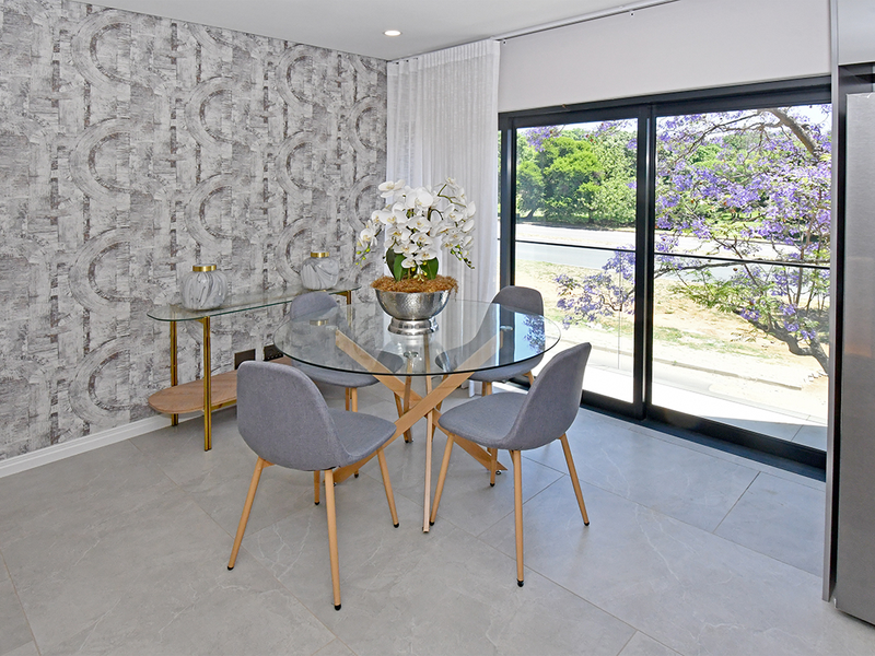 Modern dining area featuring large format floor tiles, a textured feature wall, and sliding glass doors providing natural light and garden views.