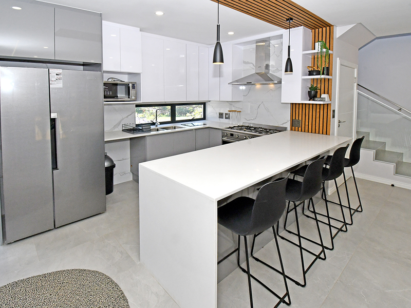 Modern kitchen featuring high-gloss cabinetry, quartz countertops, integrated appliances, a central breakfast island, and a stylish slatted timber feature wall.