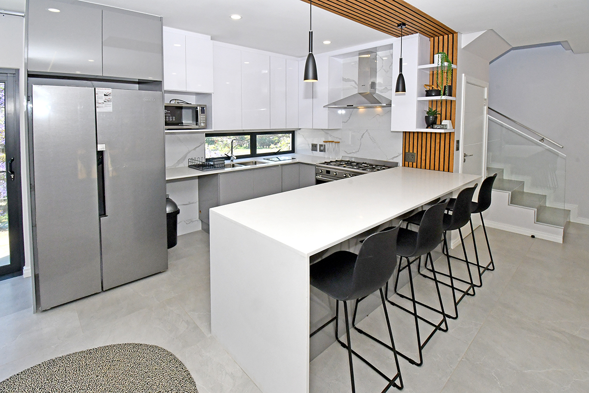 Modern kitchen featuring high-gloss cabinetry, quartz countertops, integrated appliances, a central breakfast island, and a stylish slatted timber feature wall.