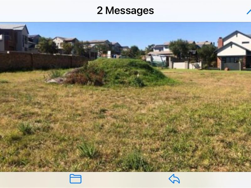 A vacant residential plot featuring natural grass cover and a central earth mound, situated within an established suburban neighborhood.