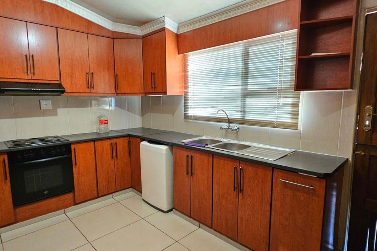 A functional kitchen featuring wood-finish cabinetry, dark countertops, a built-in oven with extractor fan, and a double-basin sink with tiled splashbacks.