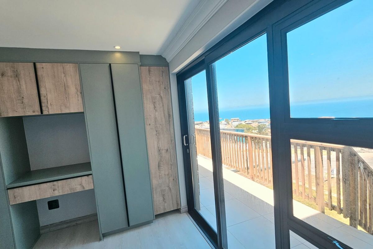 Modern bedroom featuring built-in cabinetry, a dedicated desk area, and large sliding glass doors opening onto a balcony with scenic ocean views.