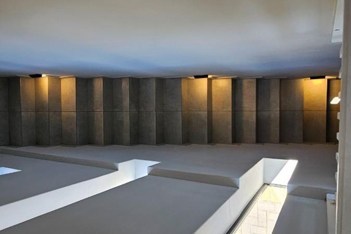 A modern interior space featuring architectural concrete wall paneling, recessed lighting, and unique floor-level skylights providing natural illumination.