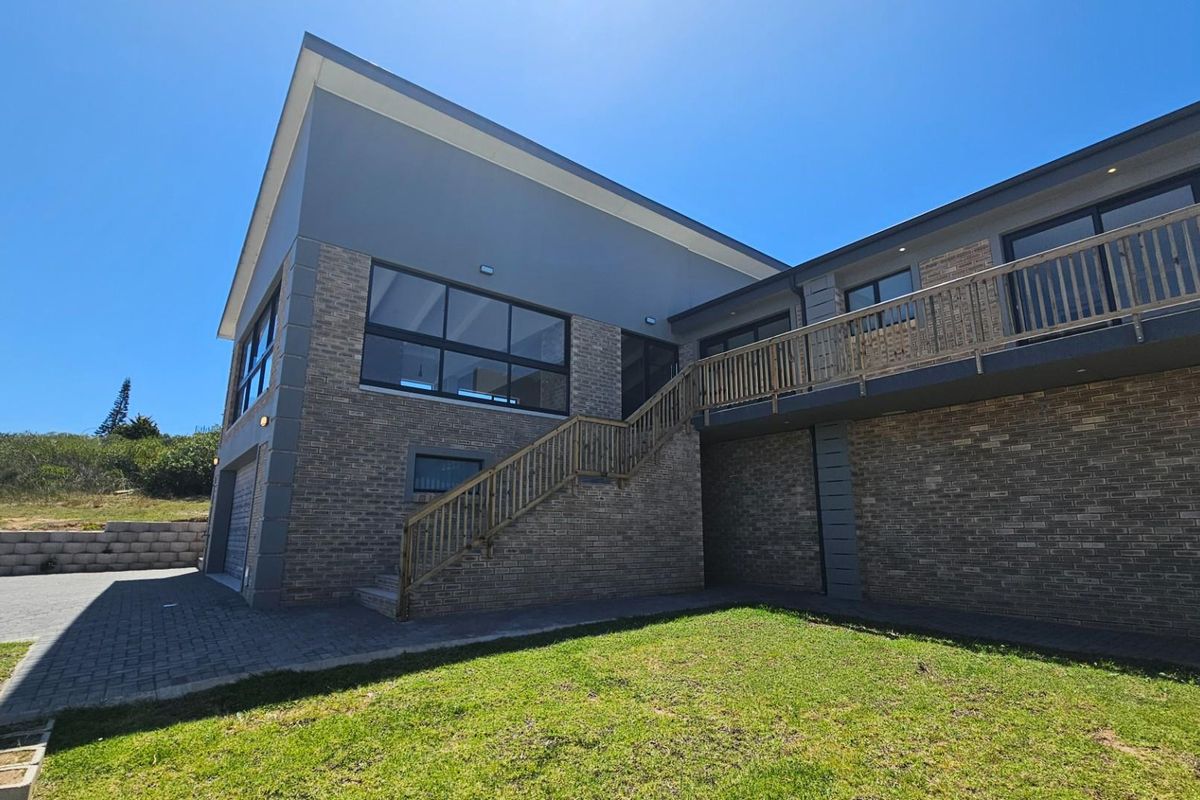 Rear view of the duet property featuring brick facade, elevated wooden deck with staircase, and paved driveway area.