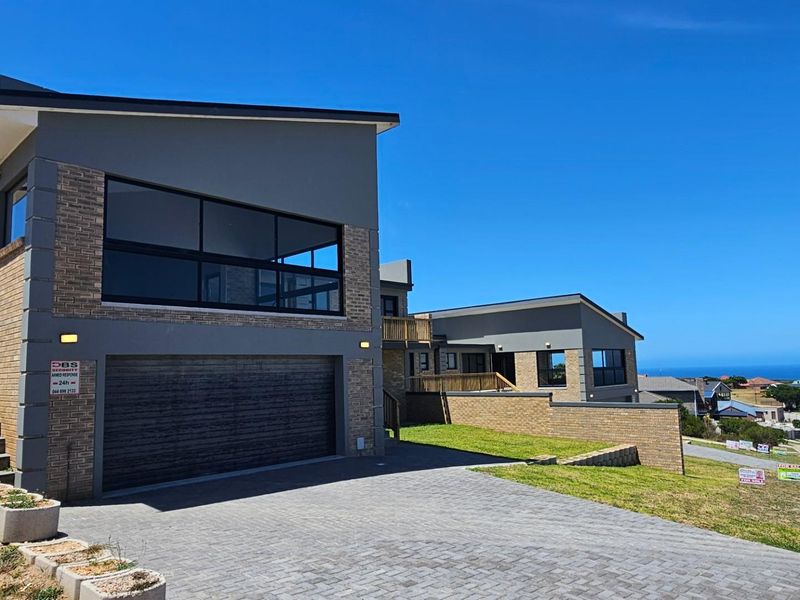 Modern duet property featuring a double garage, brick and plaster facade, paved driveway, and elevated balcony with scenic coastal views.