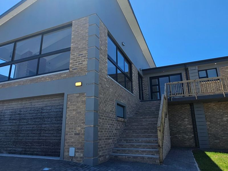 Modern duet property featuring a double garage, brick facade, and an elevated wooden staircase leading to the main entrance.