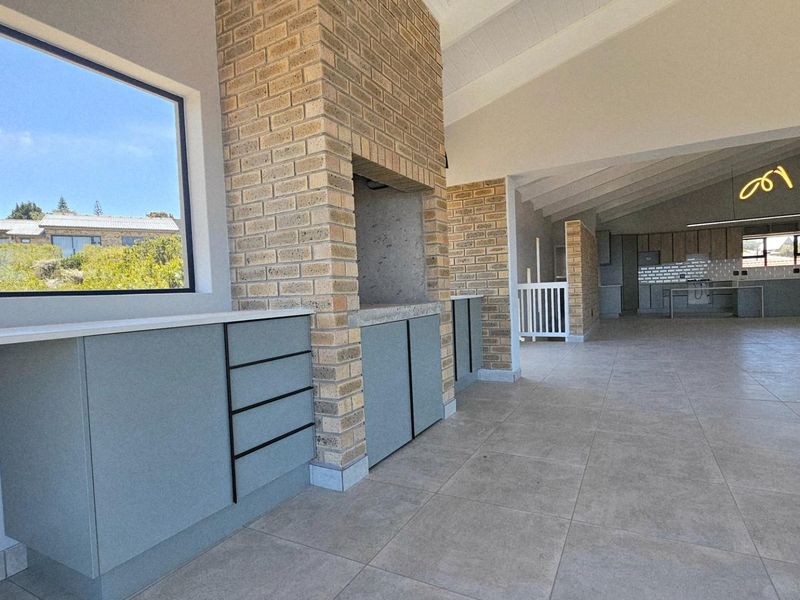 Spacious open-plan living area featuring a built-in brick fireplace, modern cabinetry, and large windows, leading into a contemporary kitchen space.