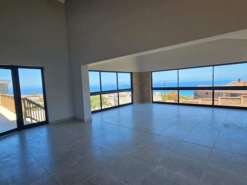 Spacious open-plan living area featuring large windows with expansive ocean views, tiled flooring, and direct access to an outdoor balcony.