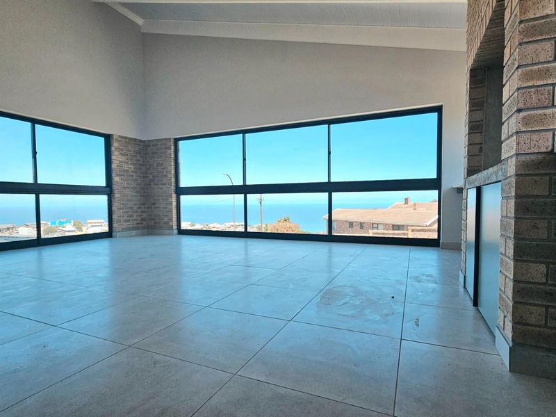 Spacious open-plan living area featuring large windows with ocean views, tiled flooring, and a built-in brick fireplace or braai area.
