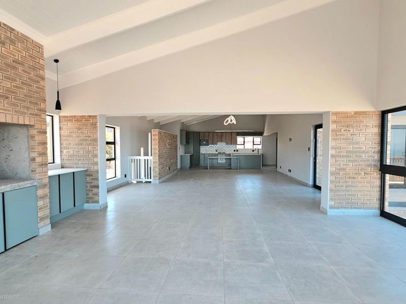 Spacious open-plan living area featuring exposed brick accents, vaulted ceilings, and a modern kitchen with integrated cabinetry and tiled flooring.