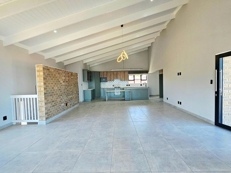 Spacious open-plan living area featuring vaulted ceilings with exposed beams, tiled flooring, and a modern kitchen with built-in cabinetry and a central island.