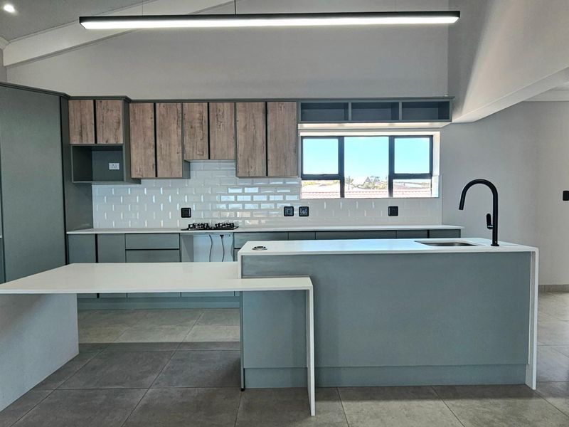 Modern kitchen featuring a central island with integrated sink, sleek cabinetry, subway tile backsplash, and a built-in hob under a vaulted ceiling.
