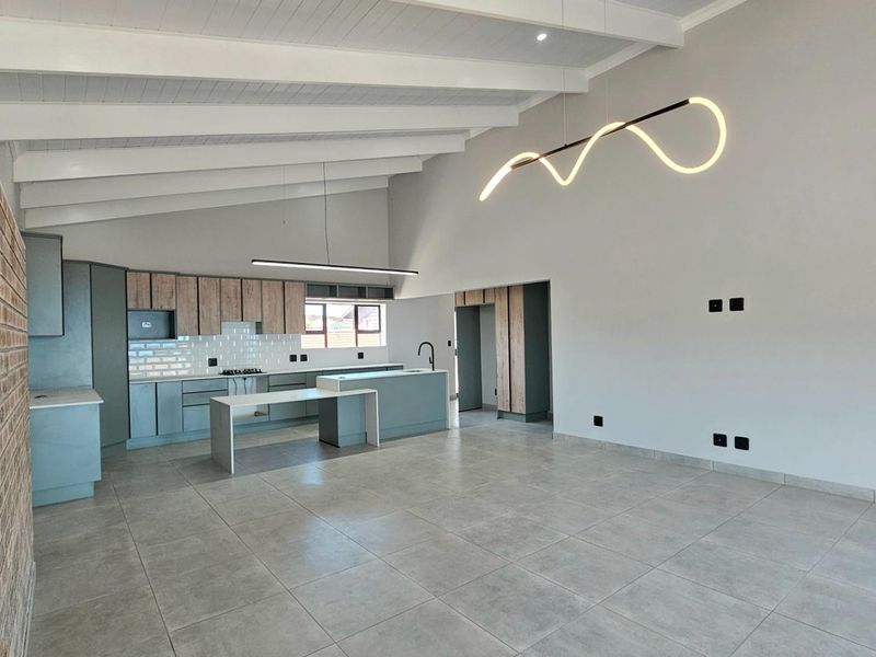 Modern open-plan kitchen and living area featuring vaulted ceilings, contemporary cabinetry, a central island, and sleek tiled flooring.