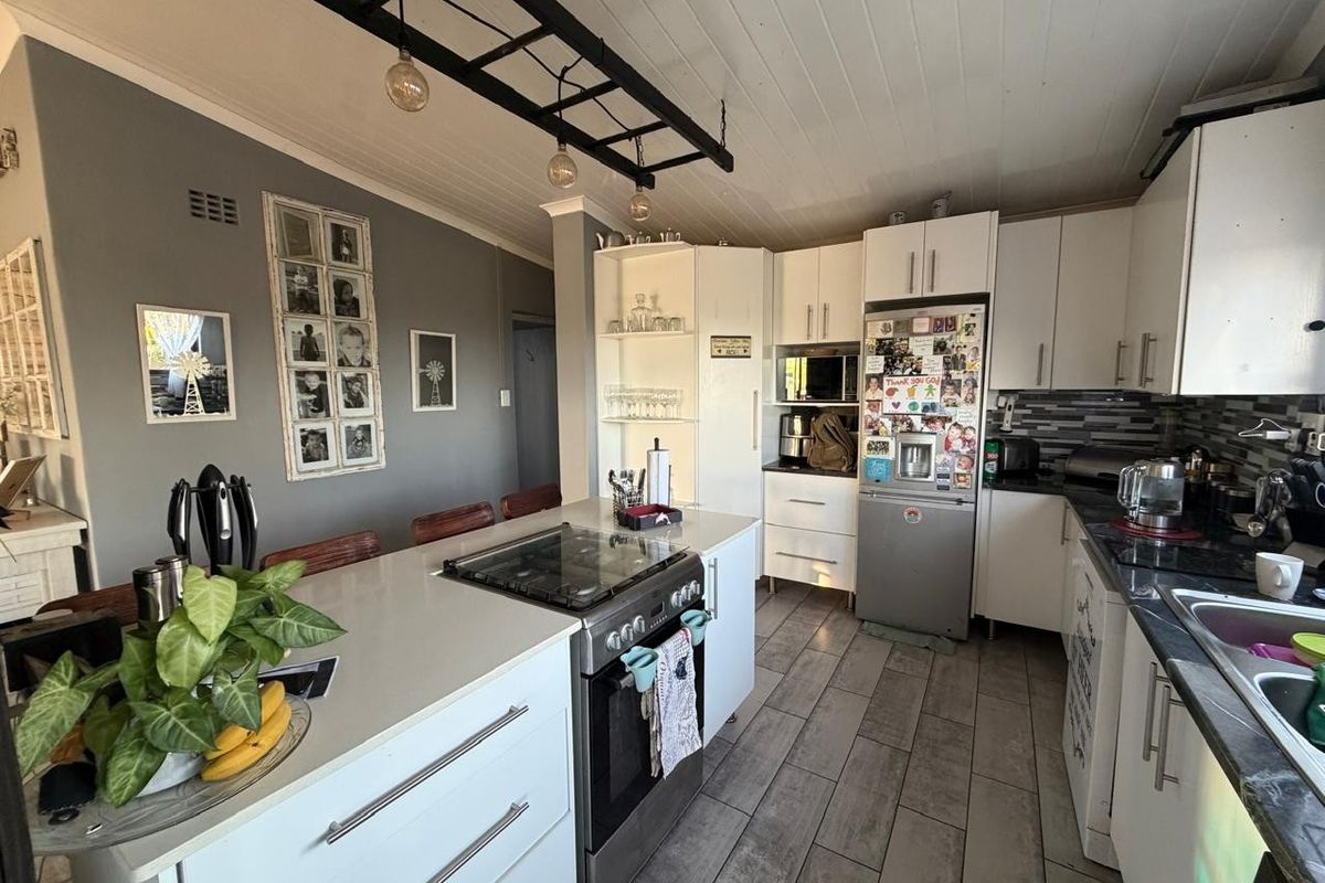 Modern kitchen featuring a central island with a gas hob, white cabinetry, stone countertops, and stylish pendant lighting, creating a functional and inviting cooking space.
