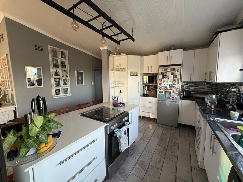 Modern kitchen featuring a central island with a gas hob, white cabinetry, stone countertops, and stylish pendant lighting, creating a functional and inviting cooking space.