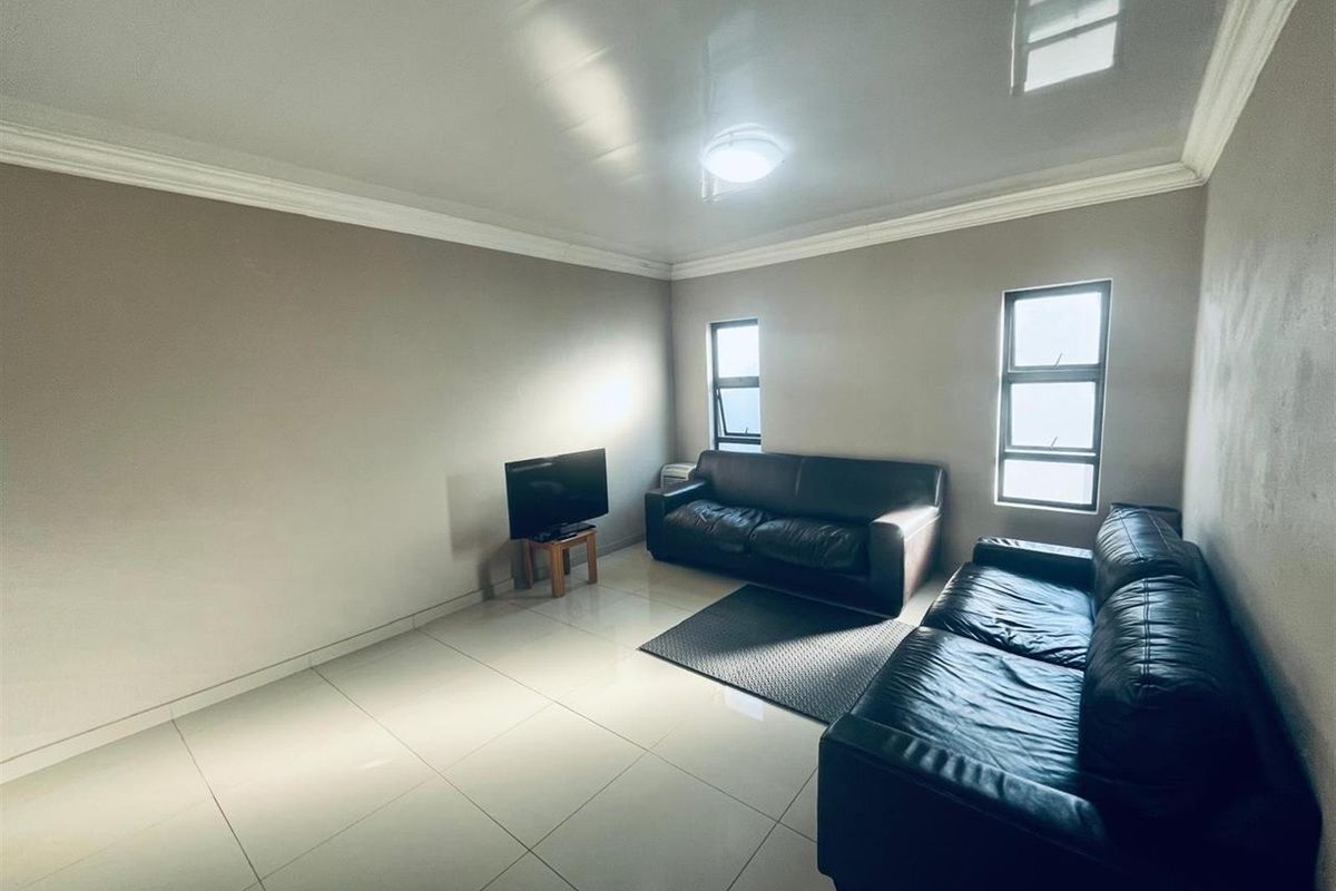 A living room featuring large format floor tiles, crown molding, and dual windows providing natural light.
