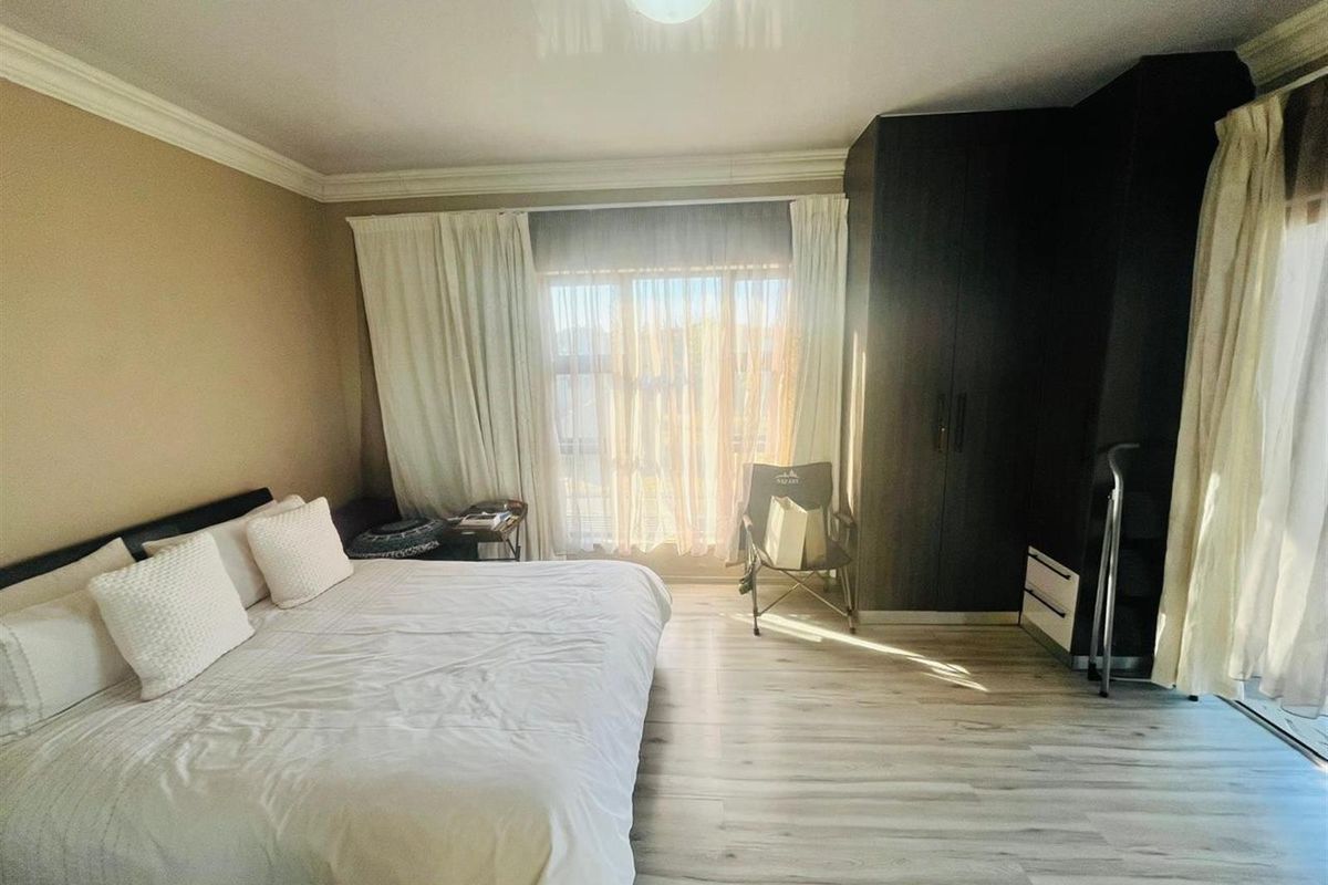 A well-lit bedroom featuring light wood-look flooring, built-in dark cabinetry, and large windows with curtains, providing a bright and functional living space.