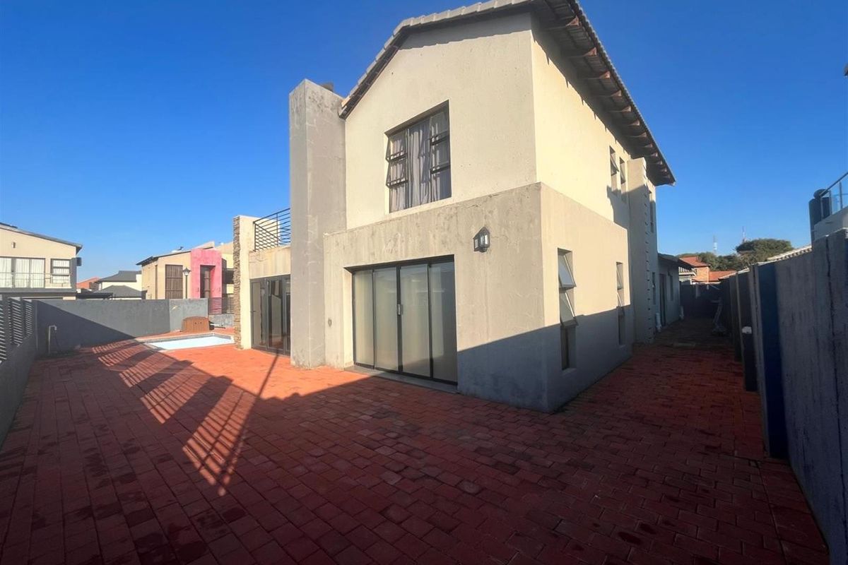 Rear view of a two-story house featuring a paved patio area, sliding glass doors, and a small swimming pool.