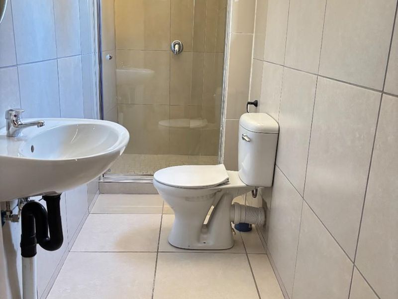 A functional bathroom featuring a pedestal washbasin, a toilet, and a glass-enclosed shower with neutral ceramic wall and floor tiling.