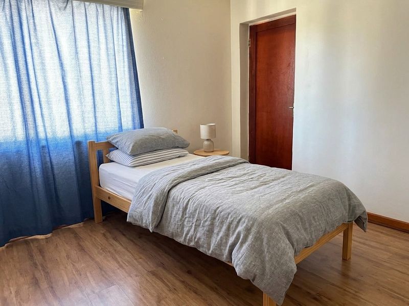 A simple bedroom featuring laminate flooring and a wooden door, providing a functional and neutral space.