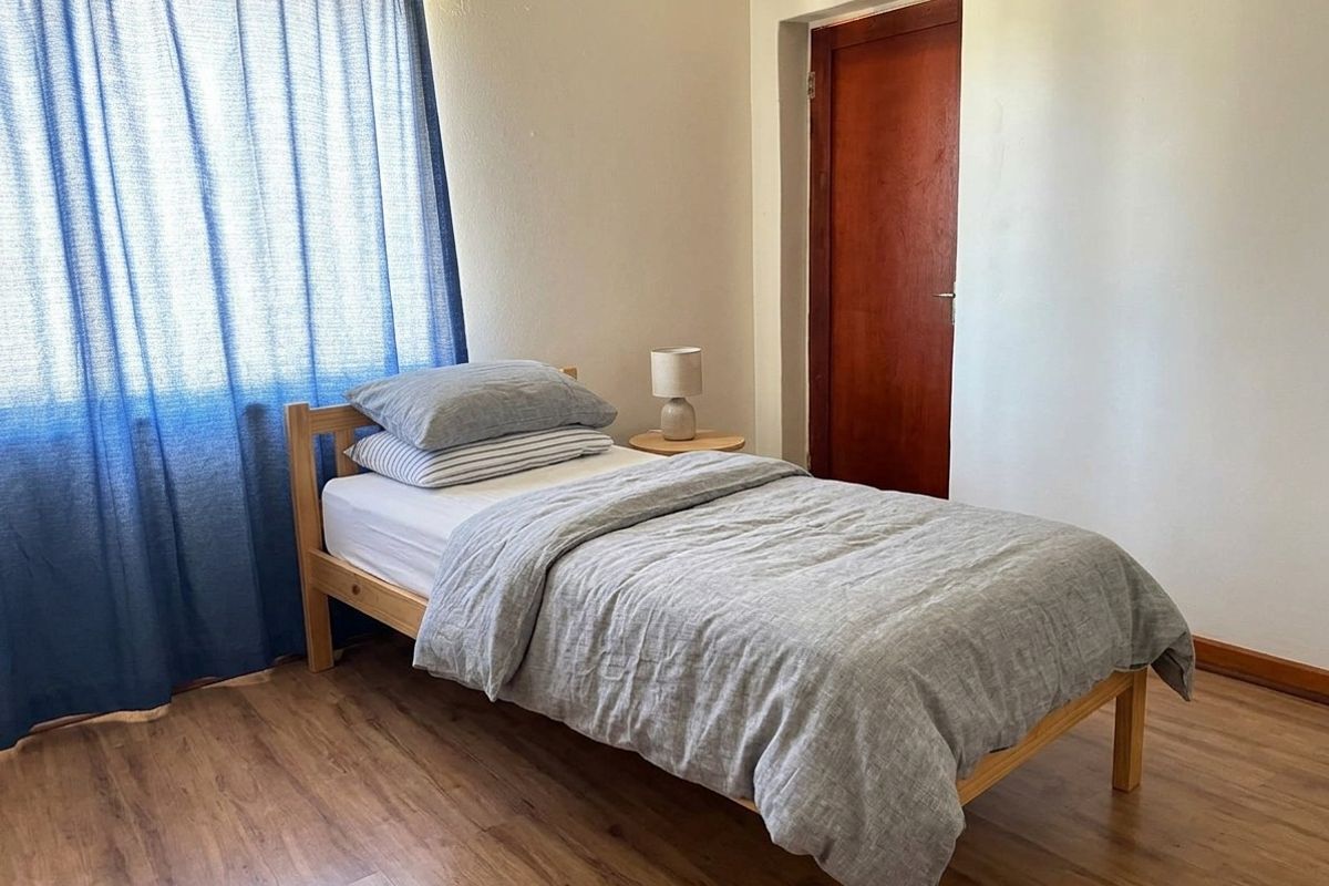 A simple bedroom featuring laminate flooring and a wooden door, providing a functional and neutral space.