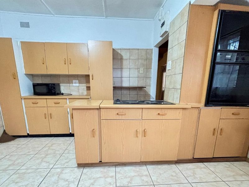 A functional kitchen featuring laminate cabinetry, tiled splashbacks, built-in oven, and electric hob with ceramic floor tiling.