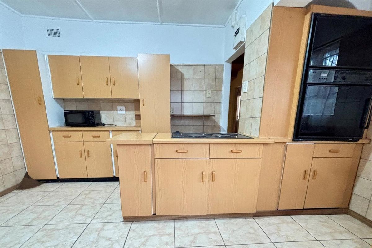 A functional kitchen featuring laminate cabinetry, tiled splashbacks, built-in oven, and electric hob with ceramic floor tiling.