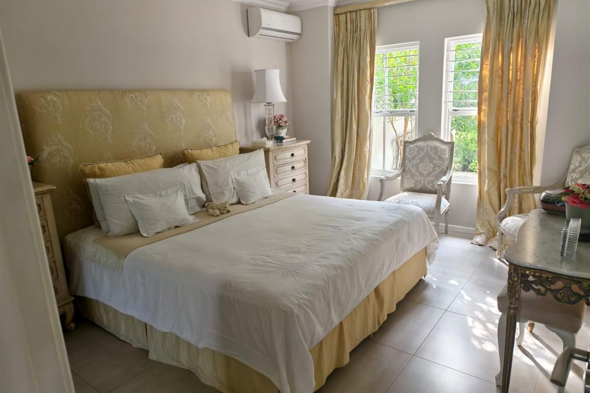 A well-maintained bedroom featuring tiled flooring, crown molding, and a wall-mounted air conditioning unit, with natural light entering through dual windows.