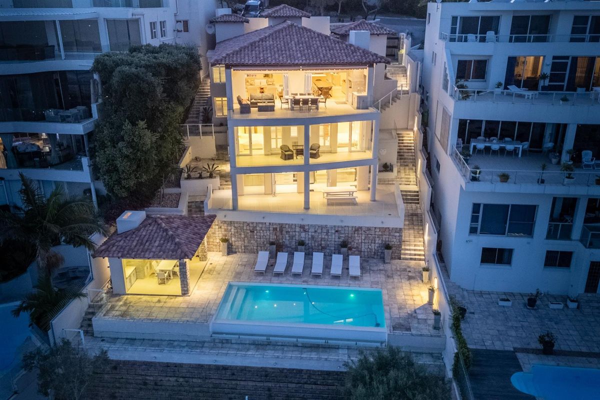 Aerial view of a multi-level residence featuring a swimming pool, stone-clad retaining walls, covered patio areas, and terracotta roof tiles at dusk.