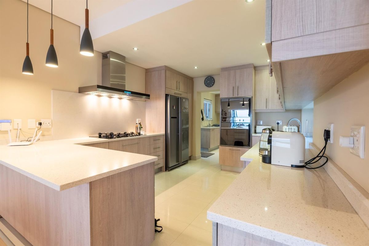 Modern kitchen featuring light wood cabinetry, stone countertops, a gas hob with extractor fan, built-in oven, and an adjoining scullery area.