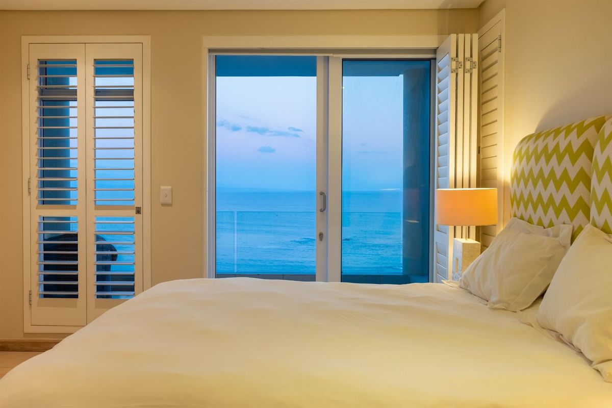 A well-maintained bedroom featuring white plantation shutters and sliding glass doors that open to a balcony with expansive ocean views.