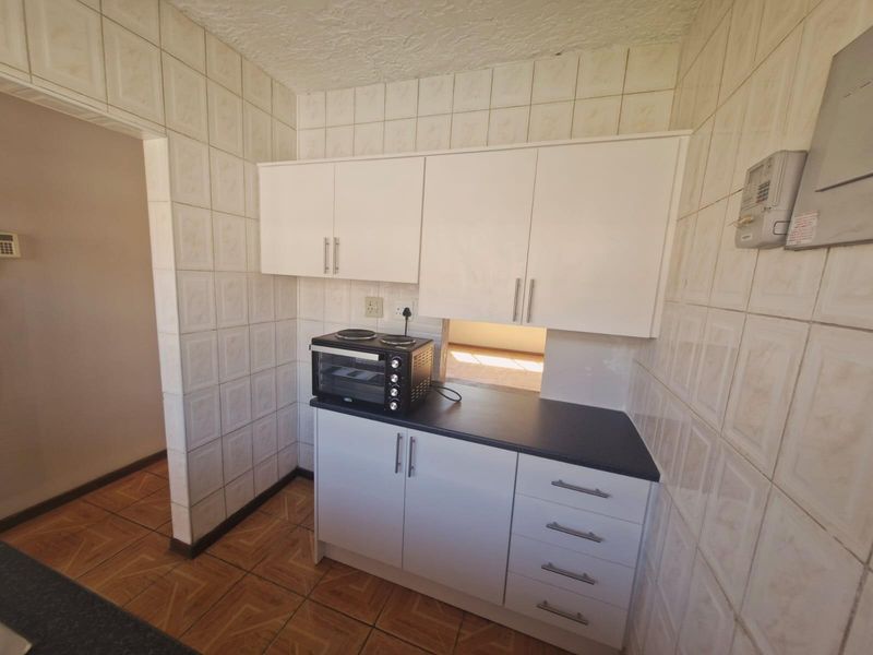 A compact kitchen featuring white built-in cabinetry, dark laminate countertops, and full-height ceramic wall tiling.