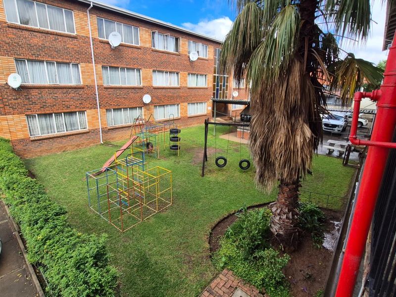 A view of the apartment complex rear exterior featuring a communal garden area with playground equipment and established landscaping.