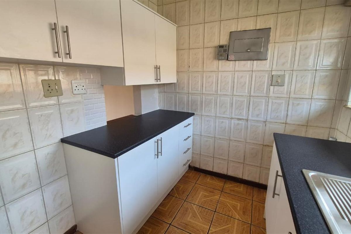 A functional kitchen featuring white cabinetry, dark laminate countertops, a stainless steel sink, and tiled wall and floor finishes.