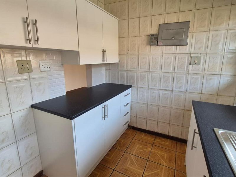 A functional kitchen featuring white cabinetry, dark laminate countertops, a stainless steel sink, and tiled wall and floor finishes.