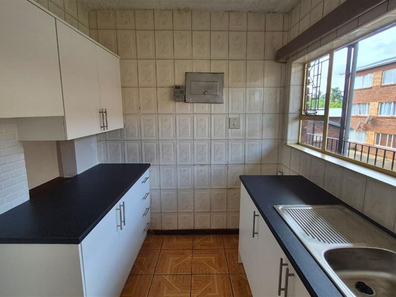 A compact kitchen featuring white cabinetry, dark laminate countertops, a stainless steel sink, and tiled finishes throughout.
