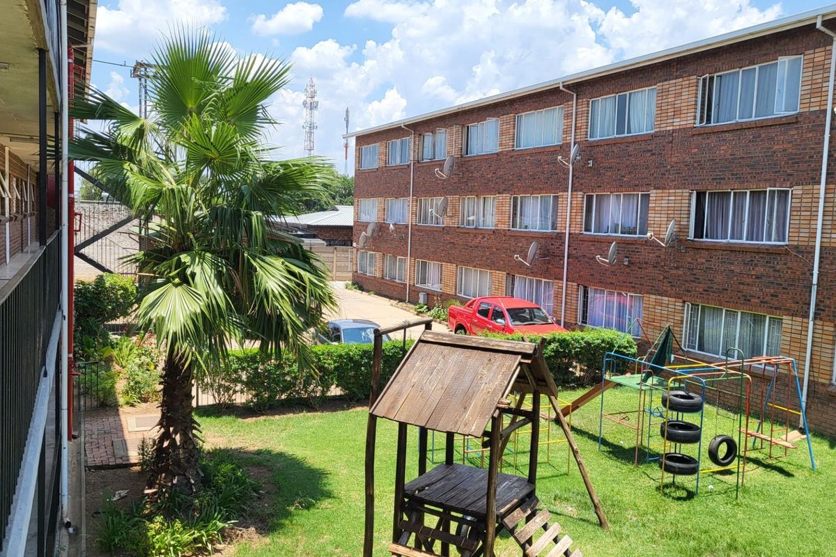 View of the apartment complex rear exterior, featuring a shared garden area, brick facade, and balcony walkways.