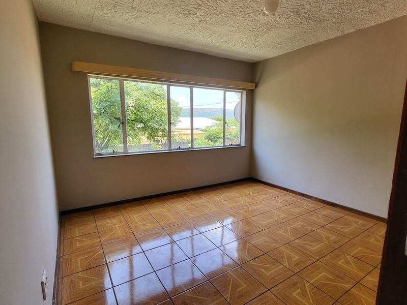 An empty bedroom featuring tiled flooring, an aluminium window frame, and a textured ceiling, offering a blank canvas for potential renovation.