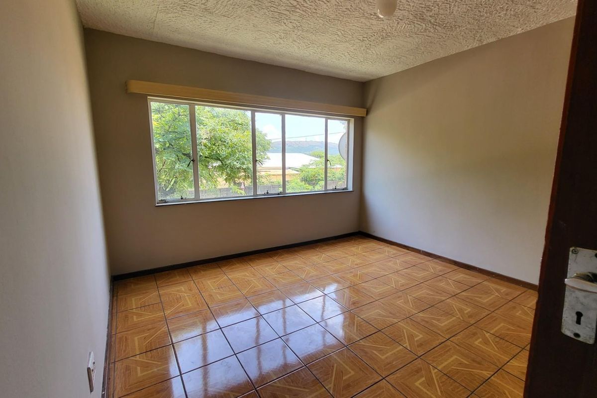 An empty bedroom featuring tiled flooring, an aluminium window frame, and a textured ceiling, offering a blank canvas for potential renovation.