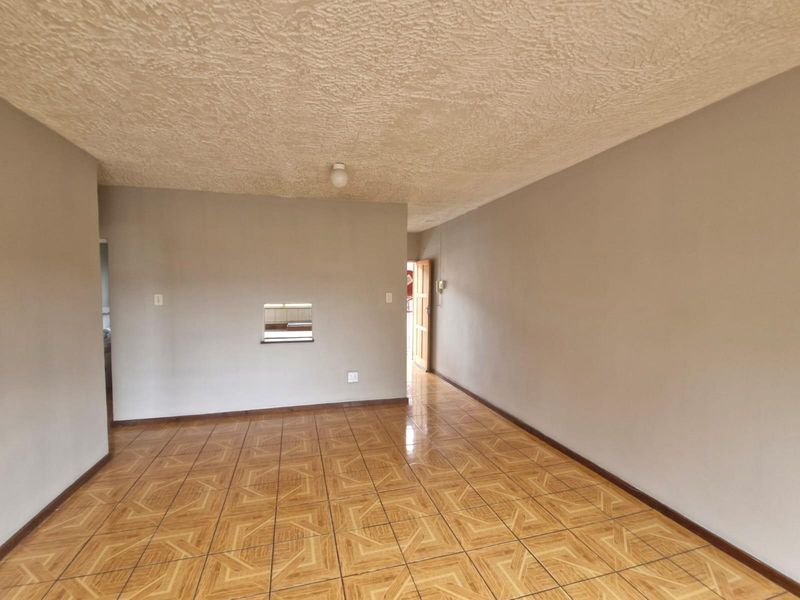 An empty living area featuring ceramic floor tiles, a textured ceiling, and a convenient serving hatch connecting to the kitchen space.