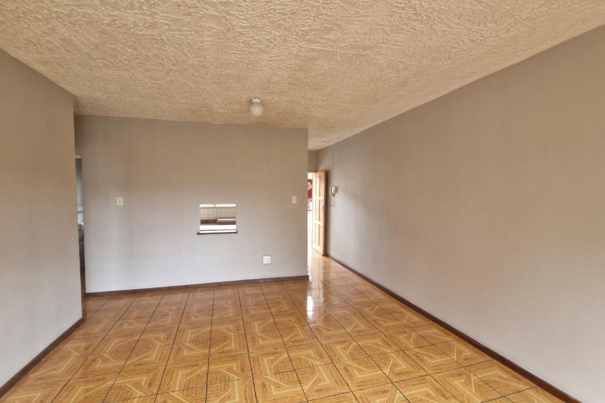 An empty living area featuring ceramic floor tiles, a textured ceiling, and a convenient serving hatch connecting to the kitchen space.