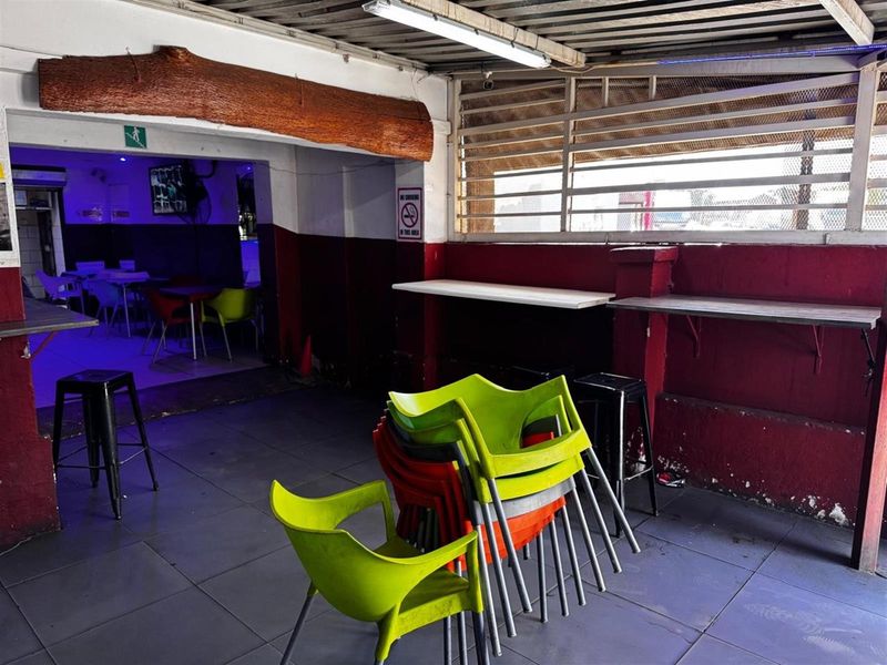 A commercial bar area featuring tiled flooring, wall-mounted counters, and metal security louvers, showing signs of wear and requiring cosmetic updates.