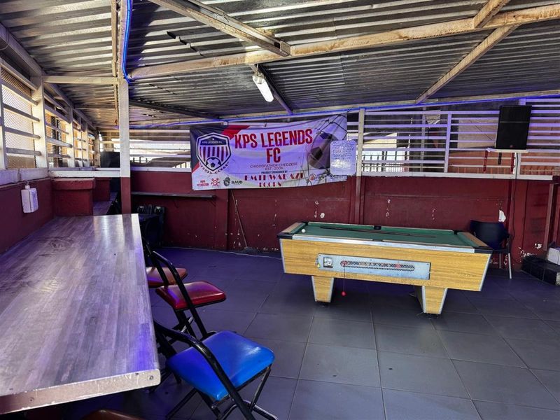 Covered outdoor entertainment area featuring tiled flooring, a fixed bar counter, and corrugated metal roofing, suitable for social gatherings or commercial use.