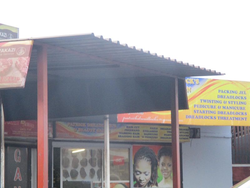 Commercial storefront featuring a corrugated metal roof canopy, steel support columns, and prominent business signage for a beauty salon.