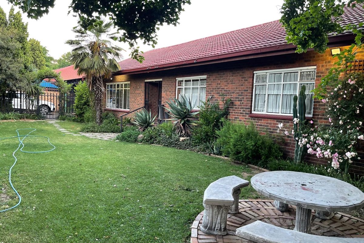 A view of the rear garden featuring a brick facade, tiled roof, and a paved circular seating area set within a landscaped lawn.