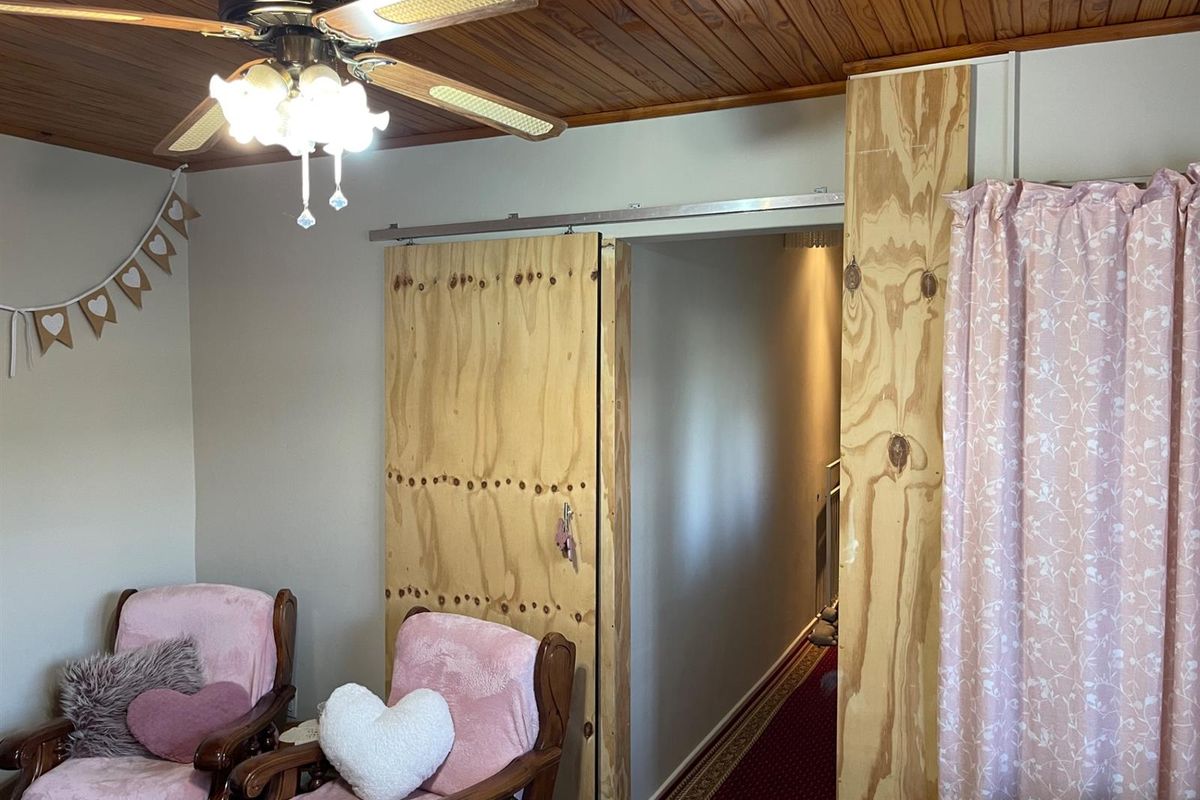 Interior view of a room featuring a timber-paneled ceiling, ceiling fan, and a custom sliding plywood door leading to a hallway.
