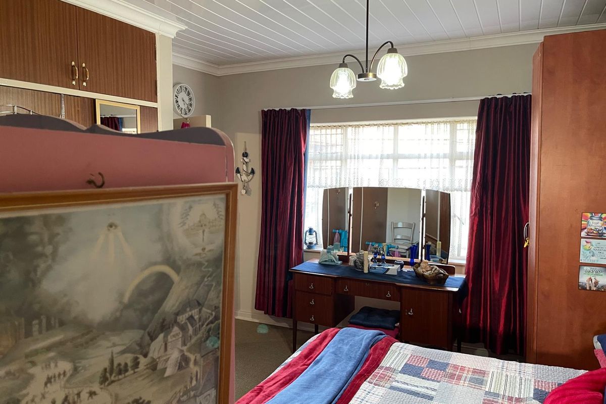 A bedroom featuring built-in wooden cabinetry, a large window with curtains, and a panelled ceiling with a central light fixture.