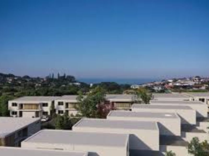 An aerial view of a modern residential apartment complex featuring flat roof architecture with a distant coastal landscape in the background.