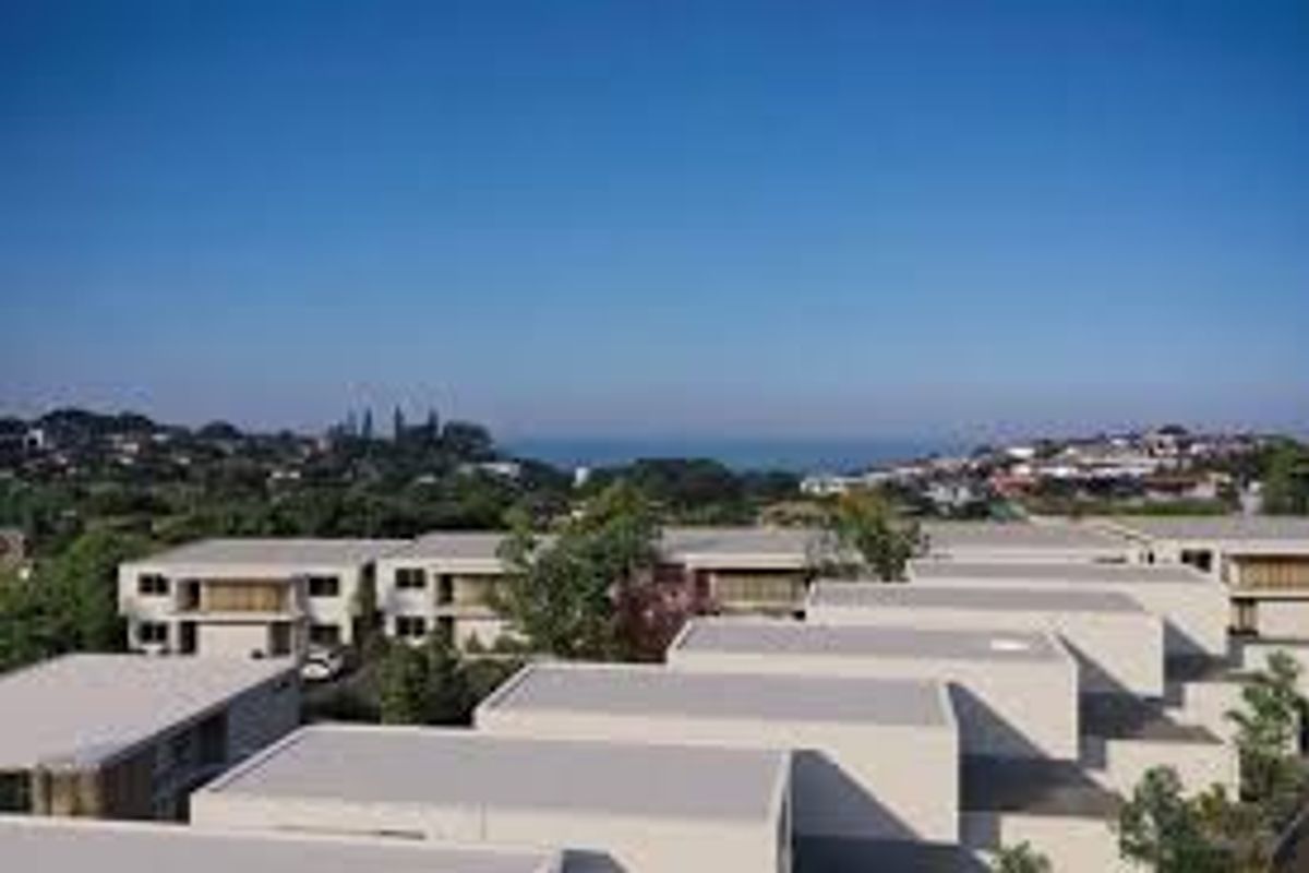 An aerial view of a modern residential apartment complex featuring flat roof architecture with a distant coastal landscape in the background.